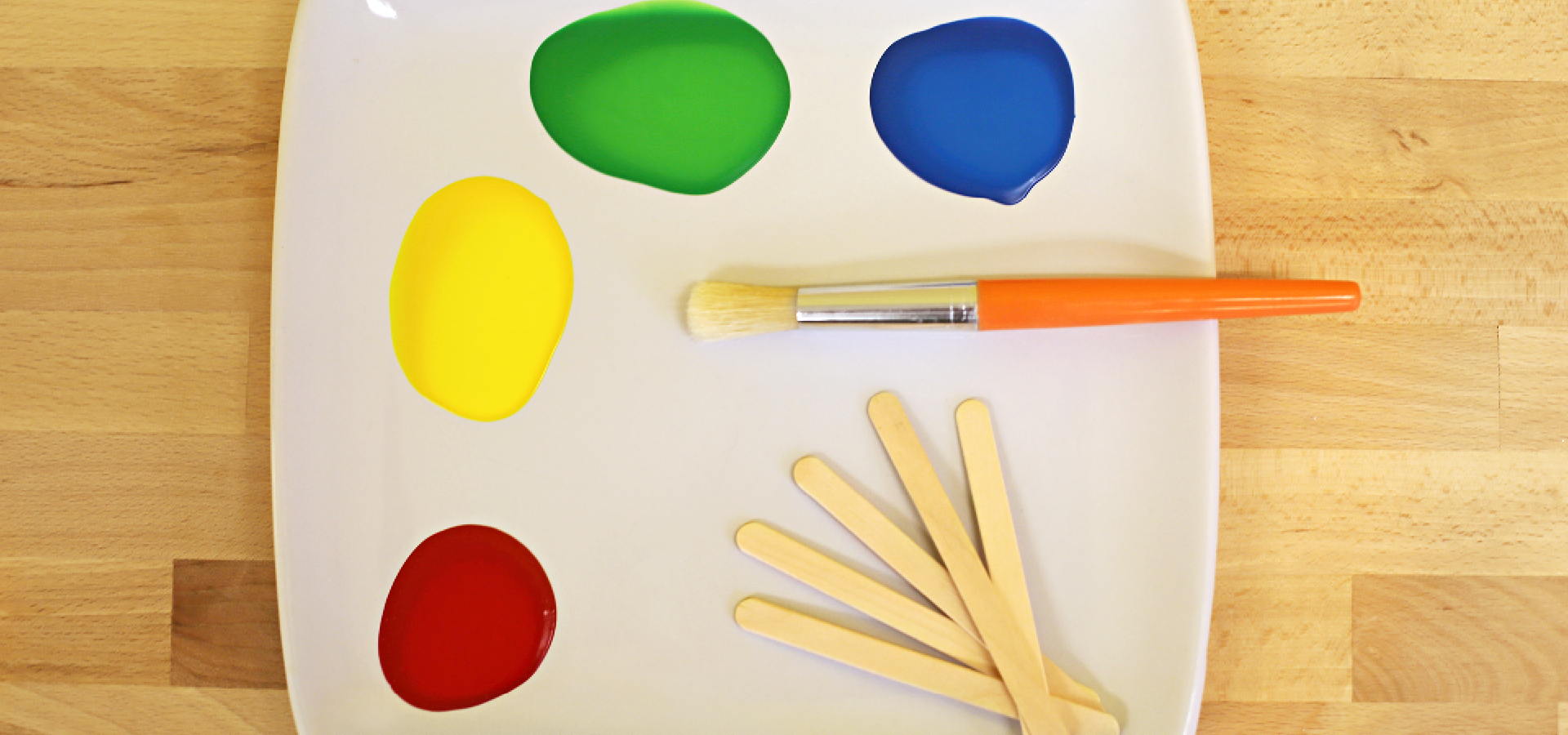 White paint tray with multicolored paints, a paintbrush, and ice pop sticks
