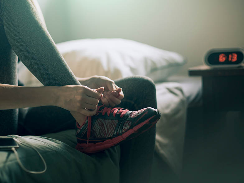 girl tying sneaker on bed