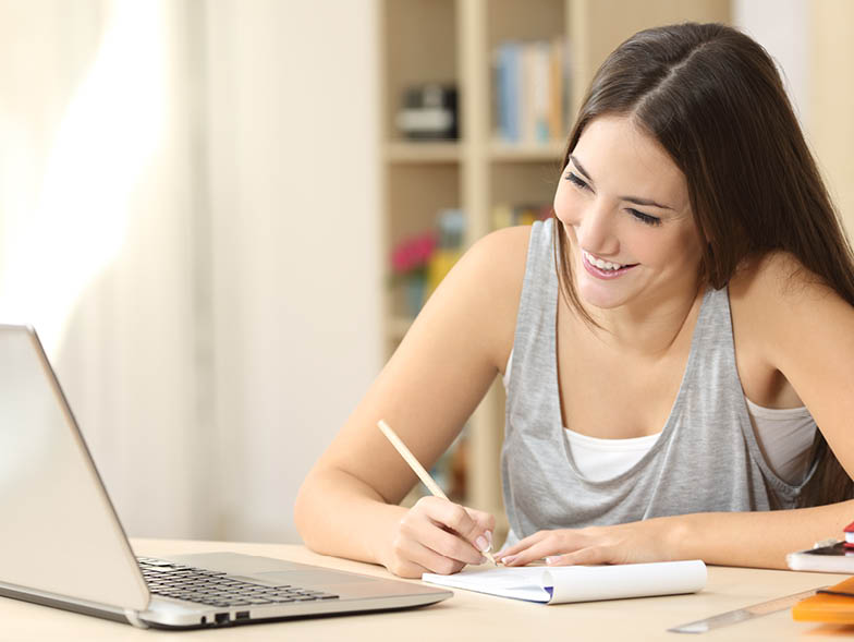 Woman writing list and looking at laptop