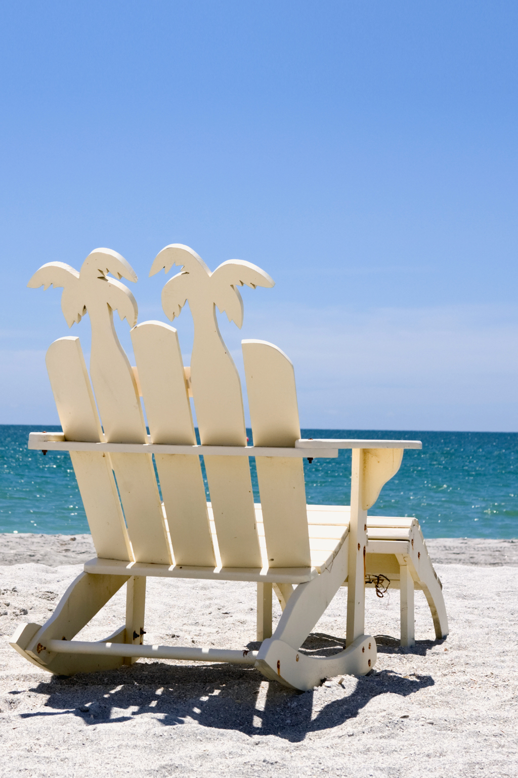Beach chair on white sand overlooking a turquoise sea.