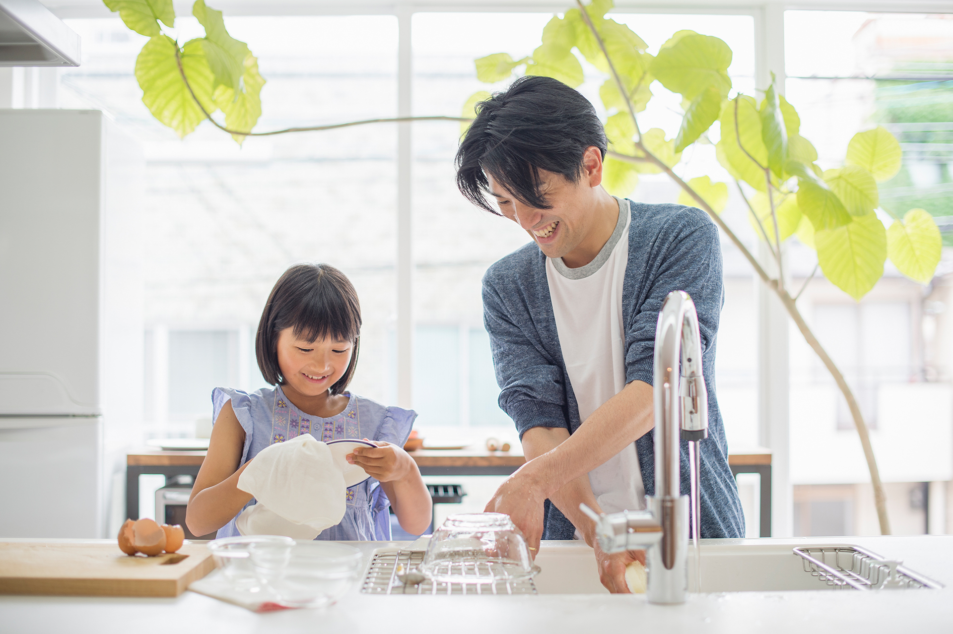 Father and daughter washing dishes in the sink together by hand