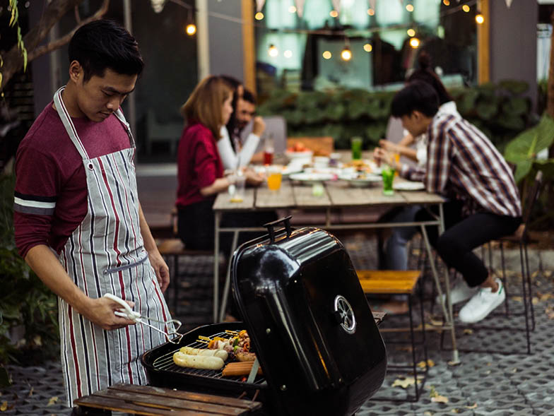 Man working grill with friends in the background