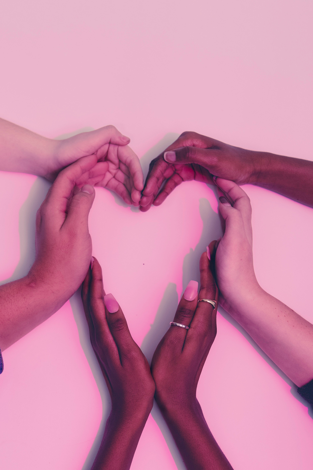 Multi-ethnic hands in the shape of a heart on a pink background
