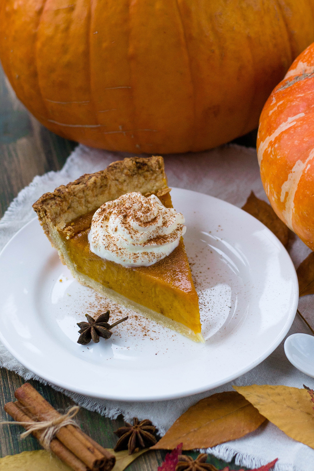 Slice of pumpkin pie with dollop of whipped cream, surrounded by pumpkins and fall decor