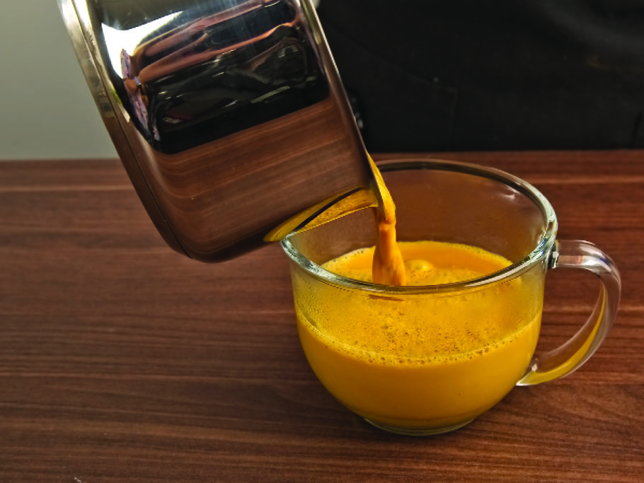 Pouring tumeric latte from pan into glass mug