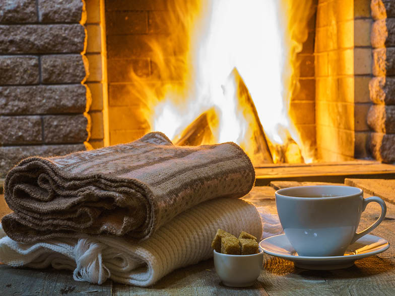 Blankets folded and a cup of tea in front of lit fireplace