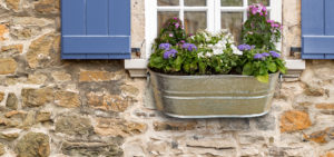 Galvanized metal flower box outside window with Red Shutters on a brick/stone wall