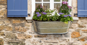 Galvanized metal flower box outside window with Red Shutters on a brick/stone wall