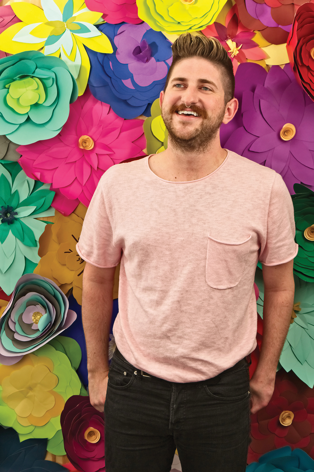 Young man smiling in front of a paper flower filled wall
