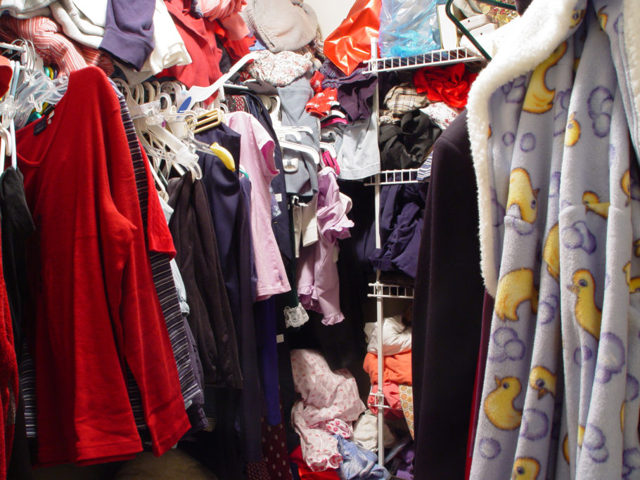 Messy closet with clothes on hangers, shelves, and just stuffed into any available space