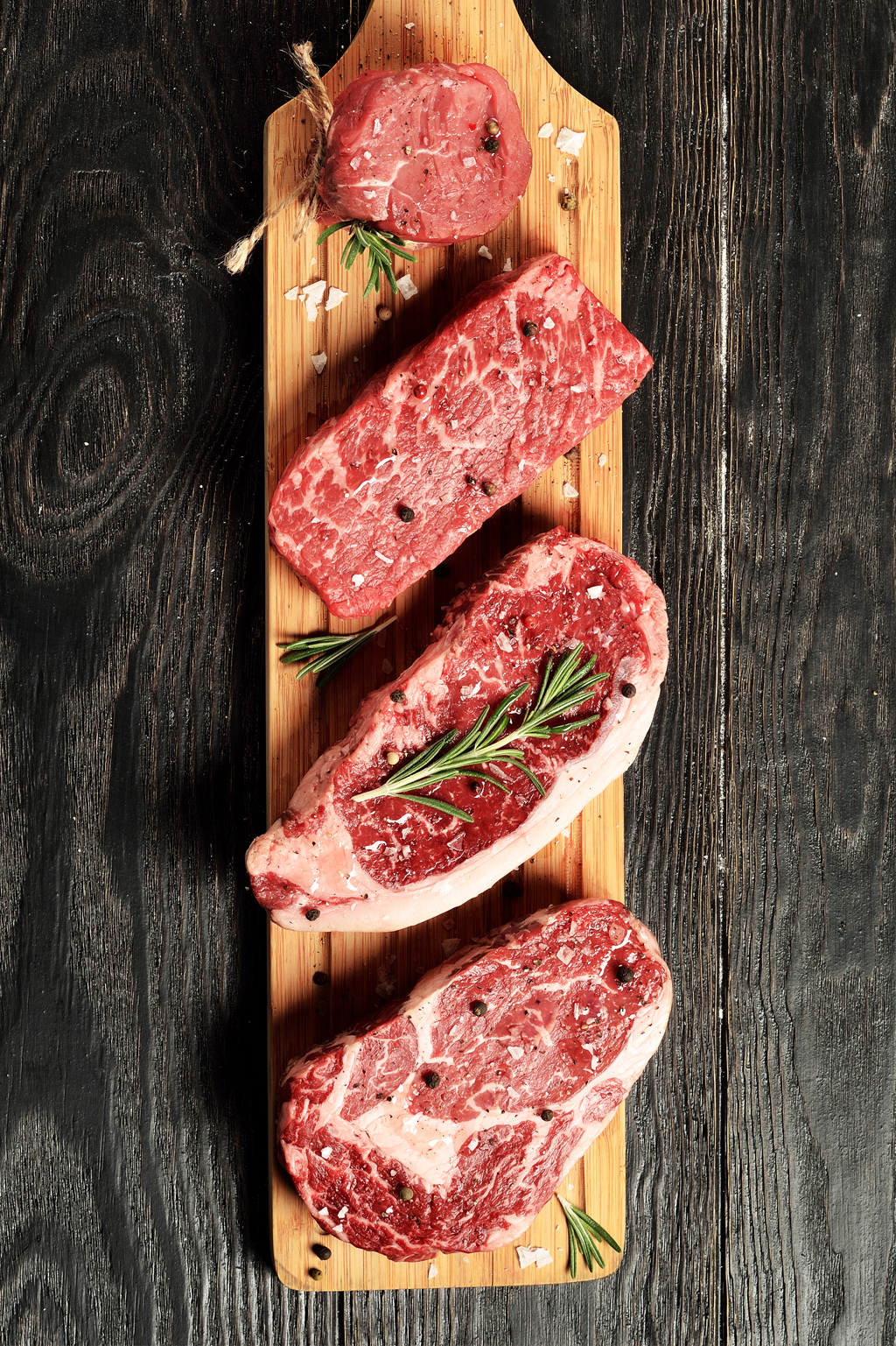 Fresh raw Prime Black Angus beef steaks on wooden board: Tenderloin, Denver Cut, Striploin, Rib Eye