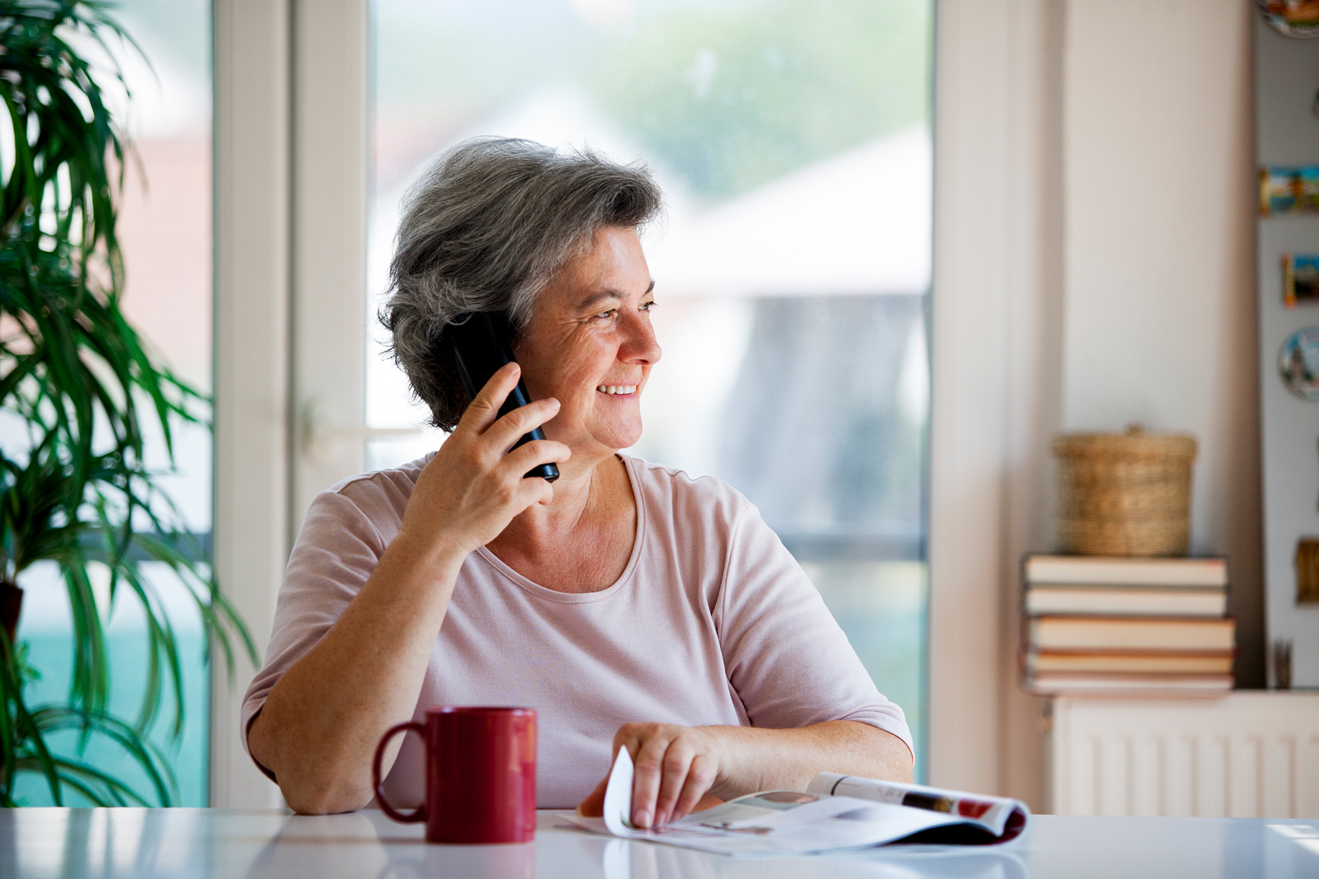 senior woman sitting at home reading magazine and talking on the phone