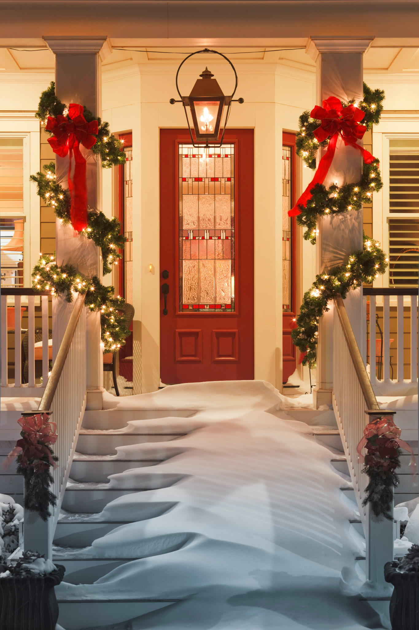 inviting Christmas doorway with snow on porch stairs and railing and lights strung along pillars