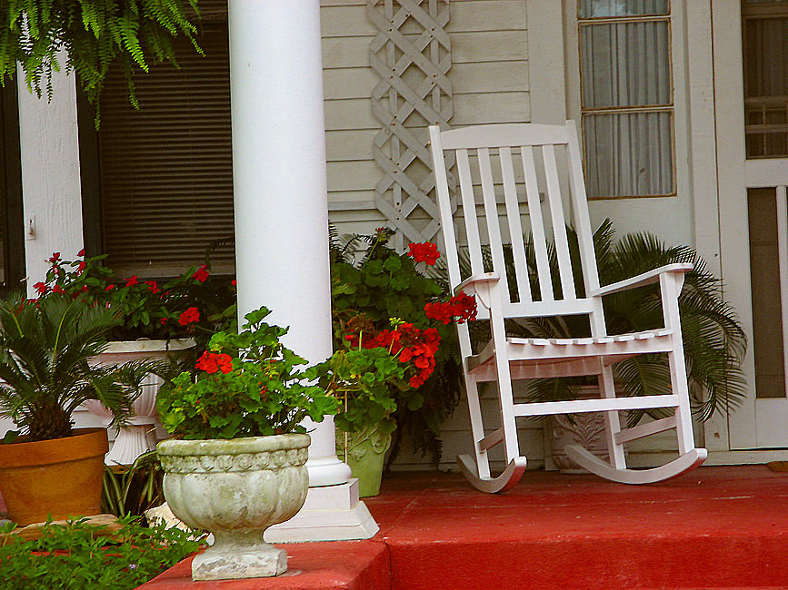 plants decorating front porch and white rocking chair