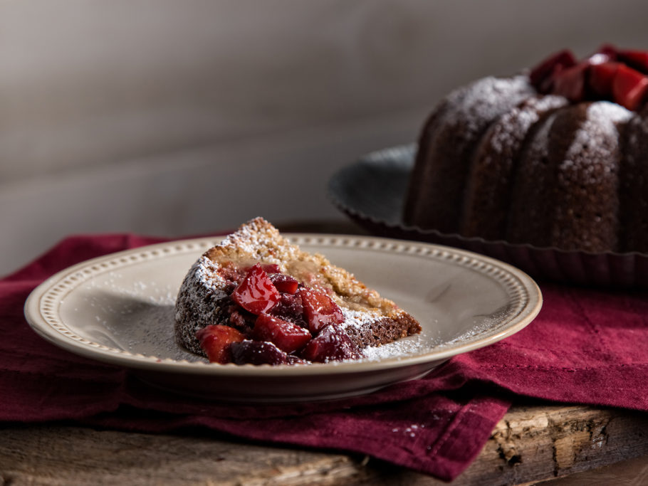 Slice of rye pound cake with plum compote and powdered sugar sprinkled atop