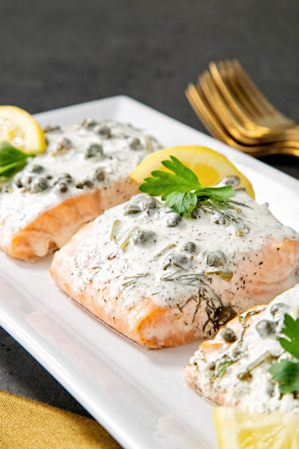 White serving tray of salmon with lemon capers and dill with golden napkin in foreground