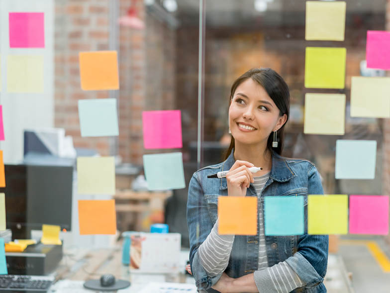 Smiling businesswoman looking at post-it notes on glass wall