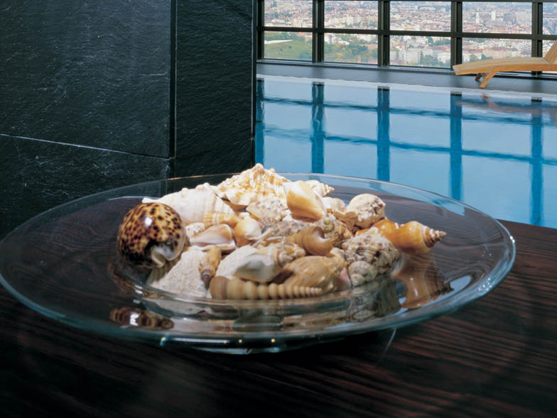 Bowl of seashells on table with pool in background