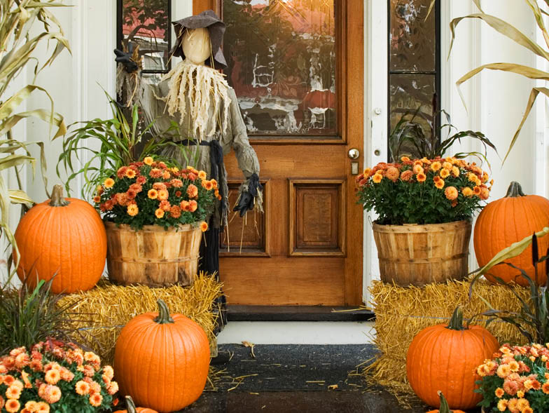 Front porch decorated with scarecrow, hay, and pumpkins
