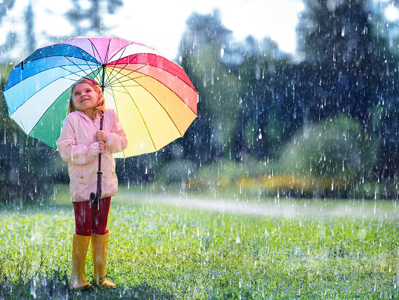 Little girl holding rainbow umbrella outside in rain