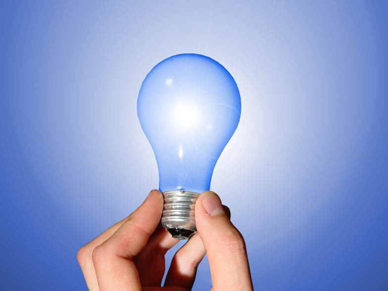 Hand holding lightbulb against blue background