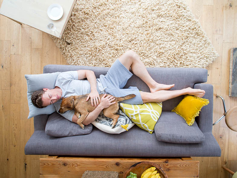Man sleeping on couch with dog laying in his arms