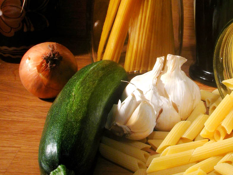 Onion, garlic, zucchini and pasta, uncooked and sitting on kitchen counter