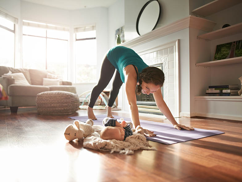 Woman doing yoga next to baby on living room floor
