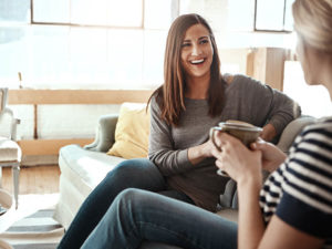 Two women drinking coffee and chatting on couch
