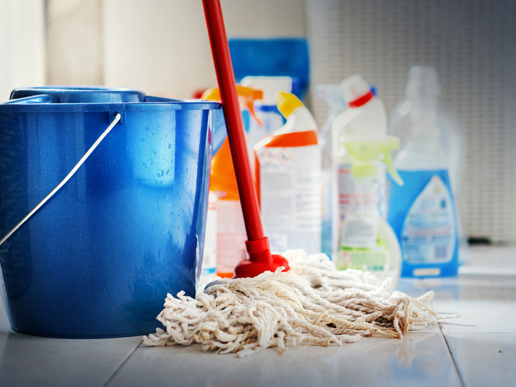 Mop with blue bucket in front of cleaning supplies