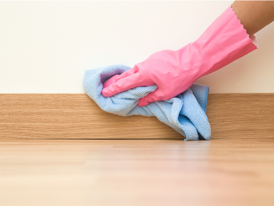 Hand wearing pink glove wiping down wooden surface with blue rag