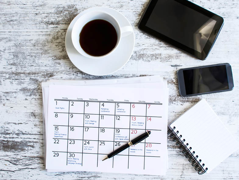 Calendar beside coffee cup, notebook, phone