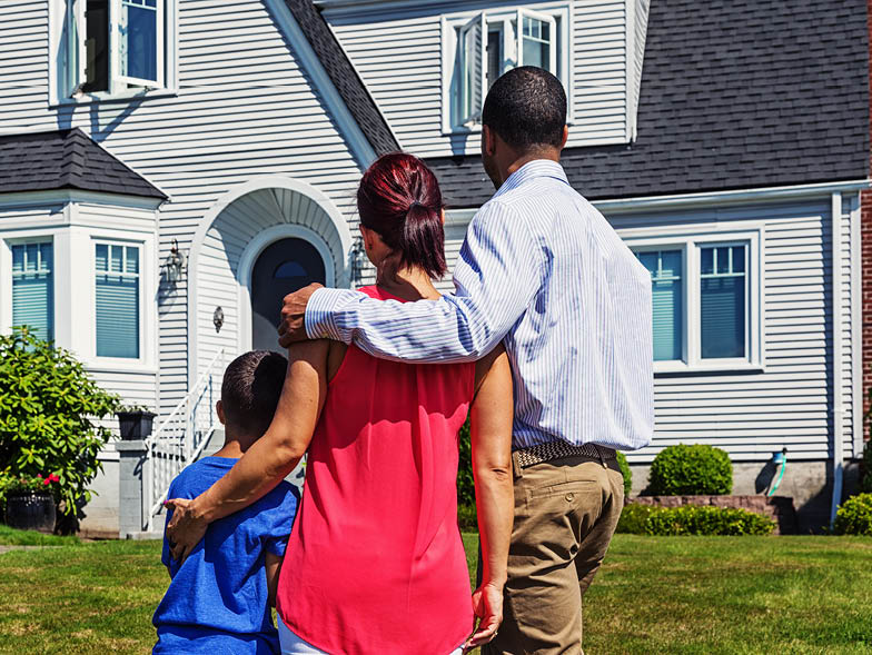 Family with arms around one another standing out front of home
