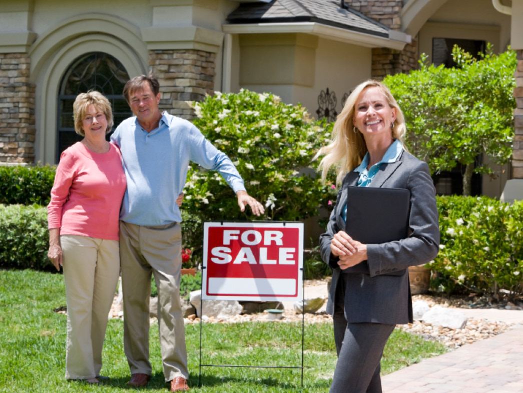 People standing in front of for sale sign at home