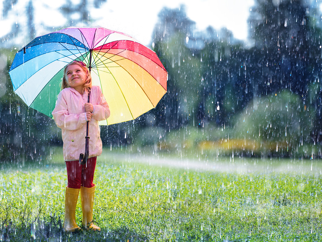 Little girl holding rainbow umbrella in the rain