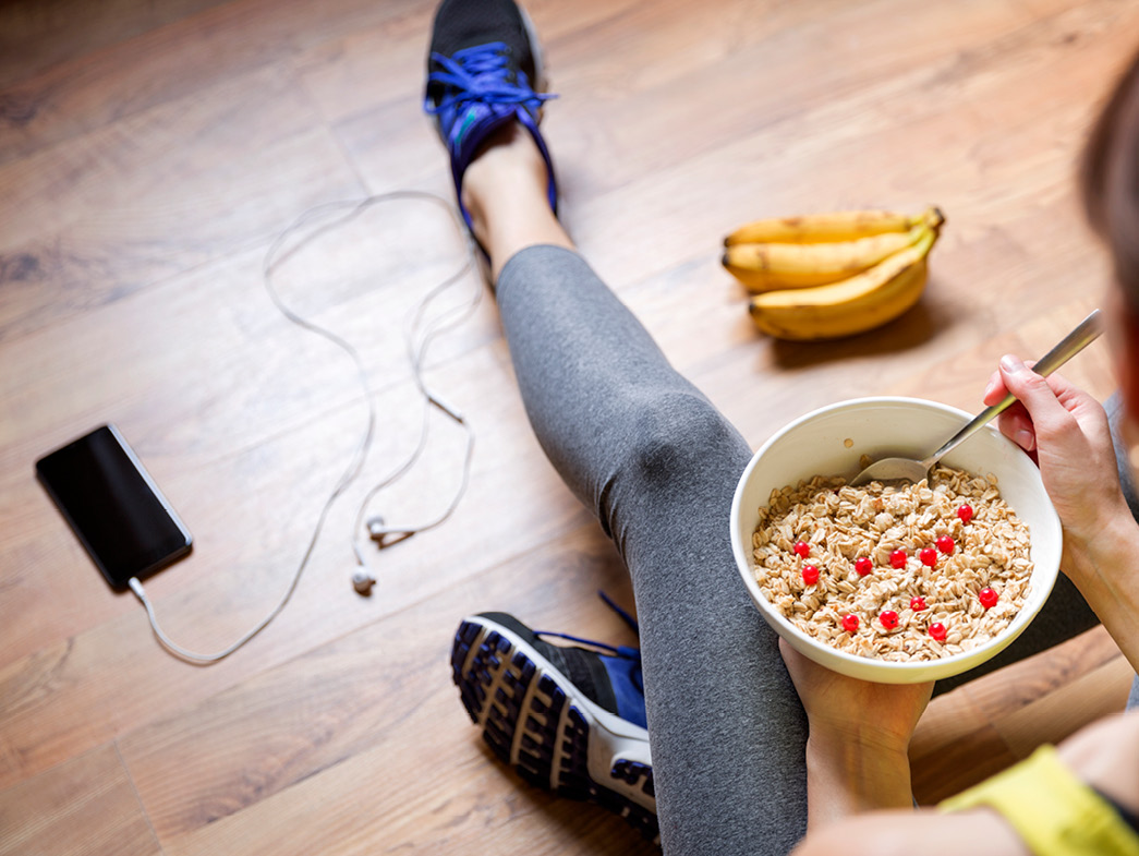 Woman sitting on floor eating cereal and bananas and wearing exercise clothing