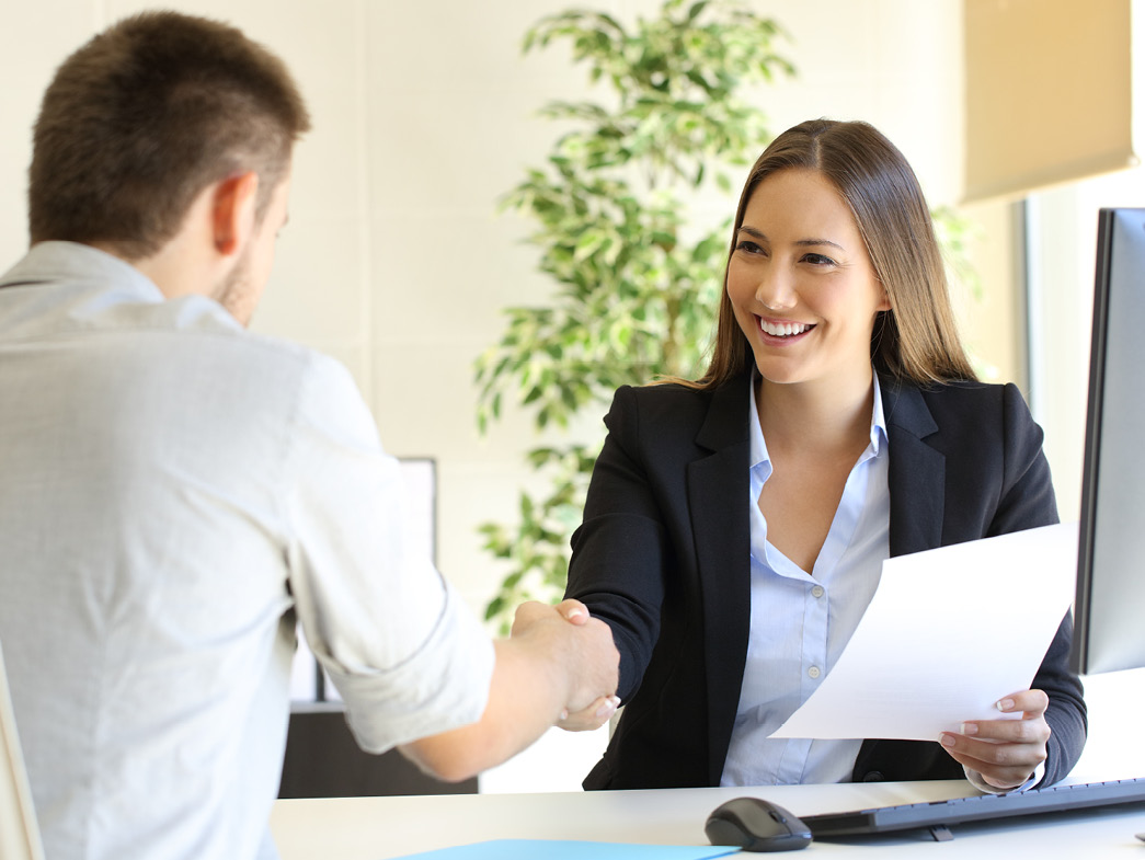 Man shaking hand with woman at computer holding papers