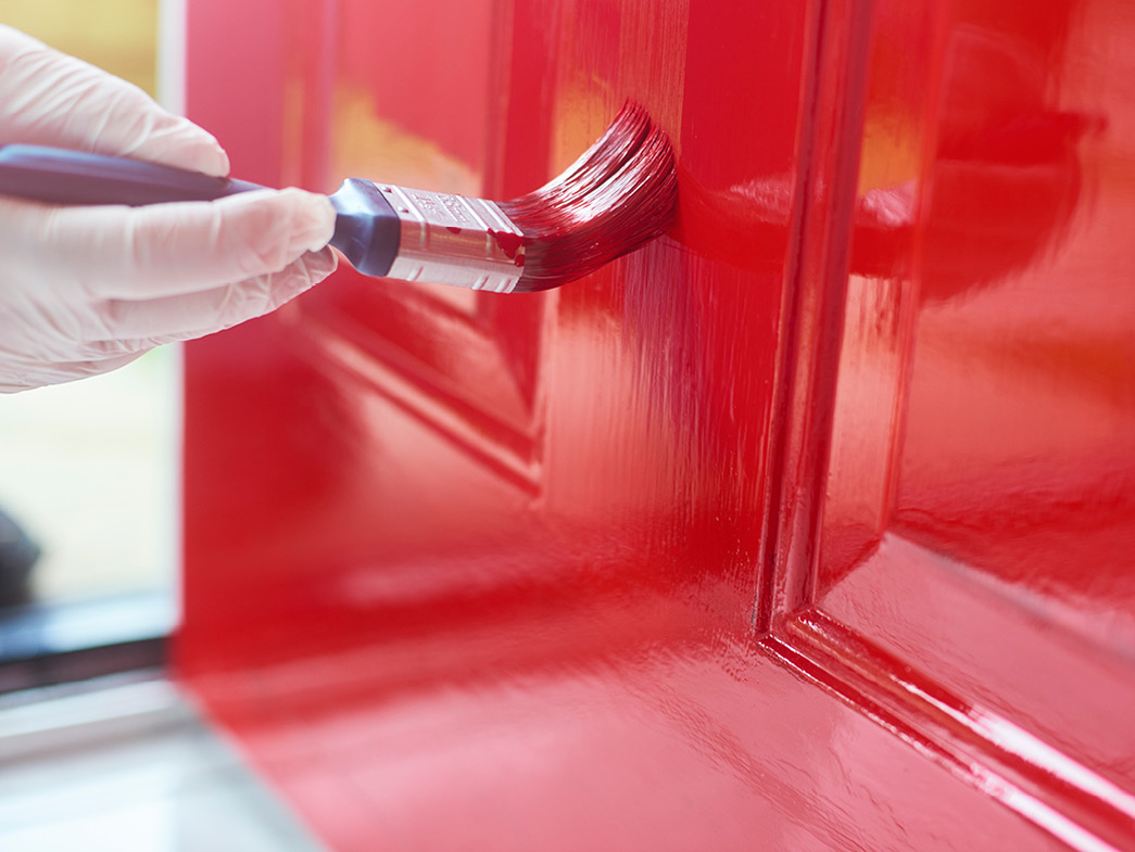 Gloved hand painting door red with small paintbrush