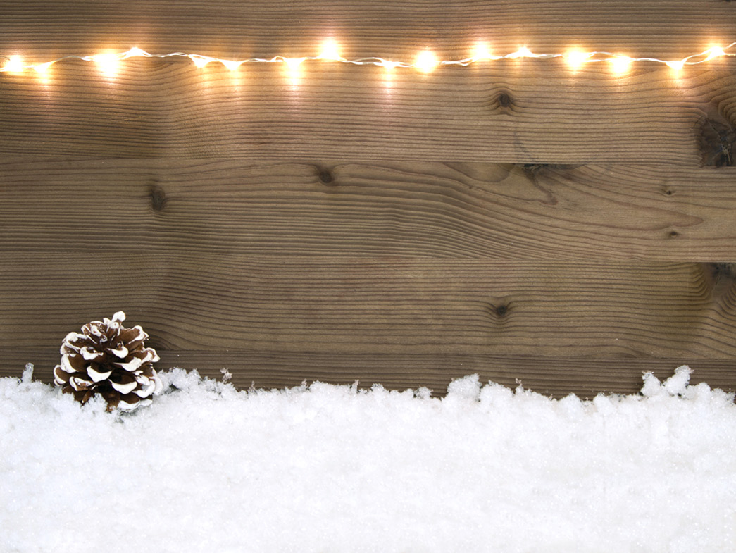 Wooden surface with white lights at the top, snow and pinecone at bottom