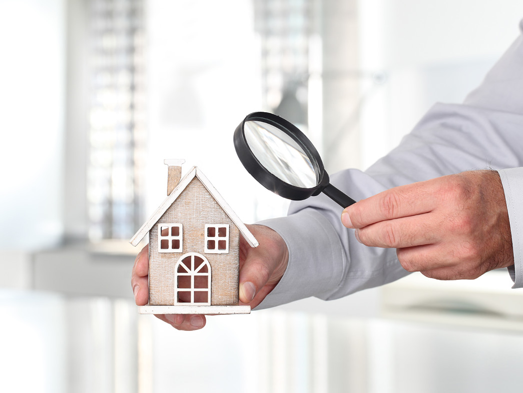 Person holding miniature house in one hand and a magnifying glass in the other