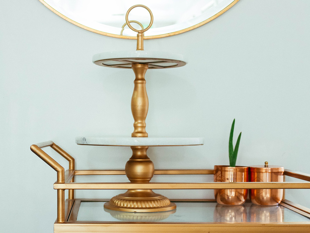Gold items on cart below gold rimmed mirror