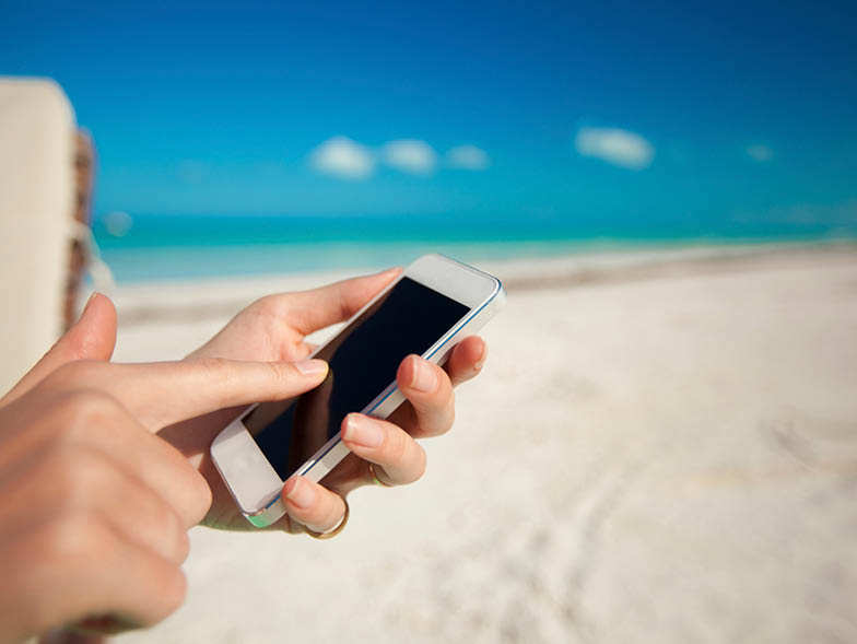 Person tapping phone screen with beach in background