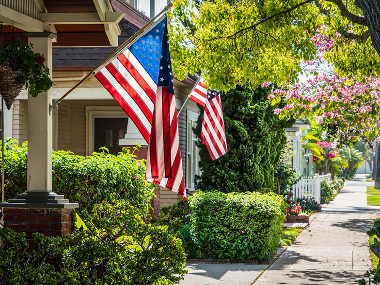 View from sidewalk of nice neighborhood in summer, with American flags hanging on front porches