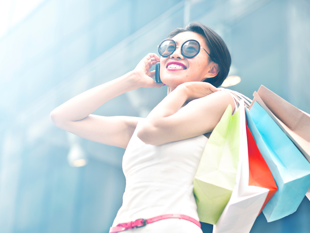 Woman holding shopping bags over shoulder with cell phone up to her ear
