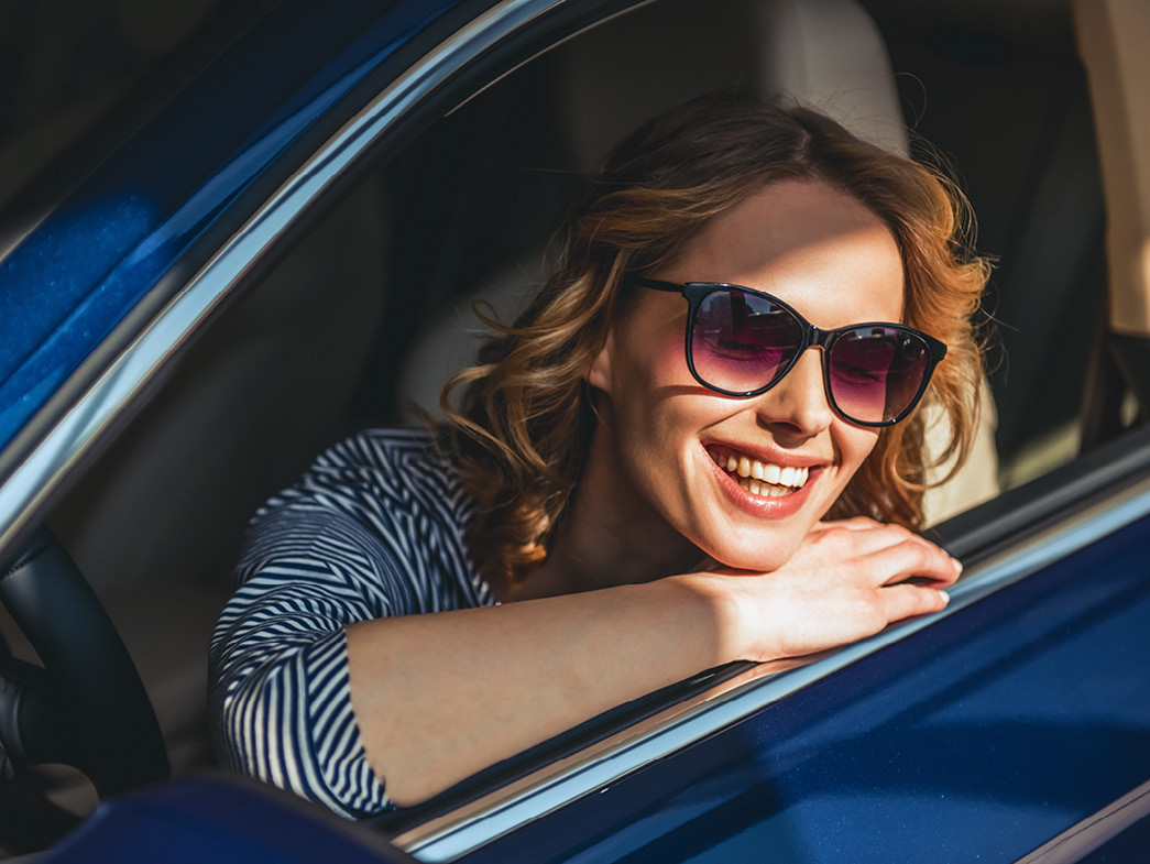 Woman with sunglasses smiling and resting head on car window