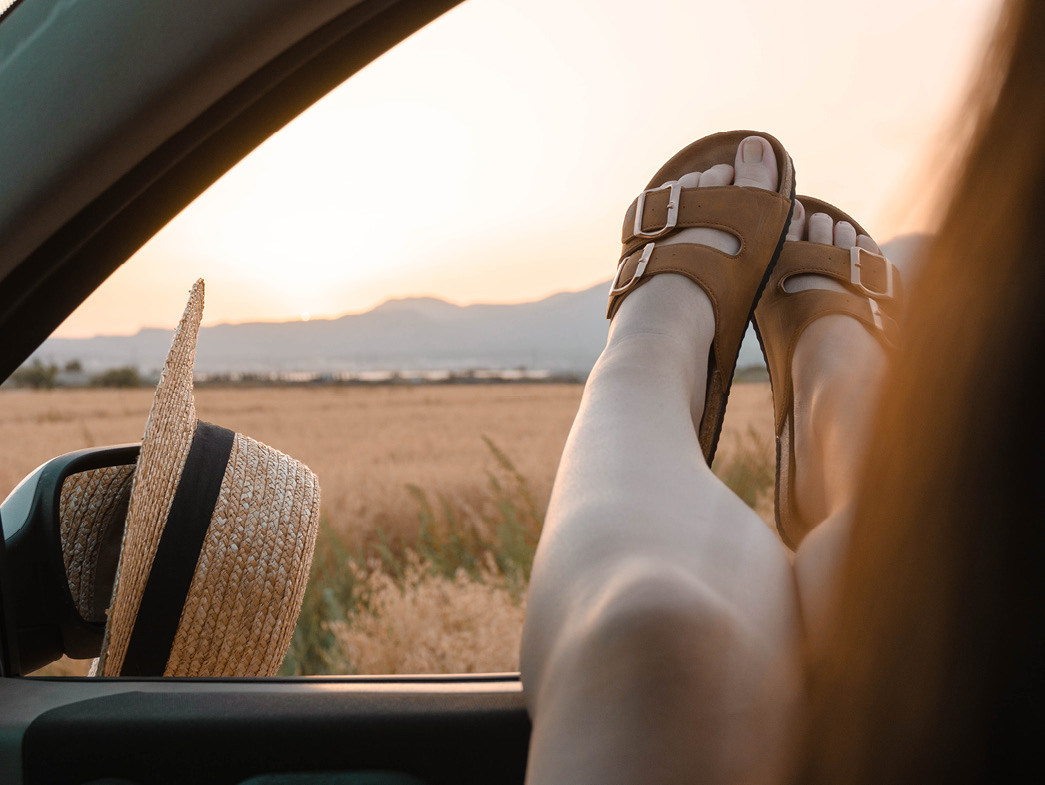 Woman in sandals hanging feet out of car window