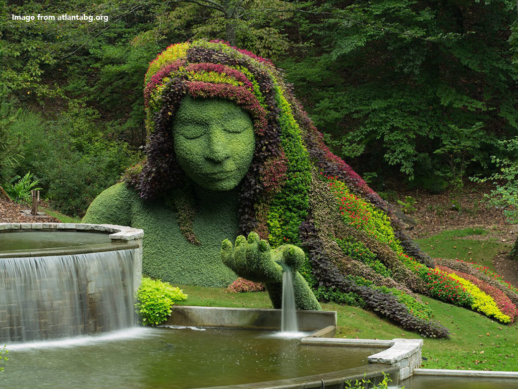 Sculpture of woman made out of plants beside fountain