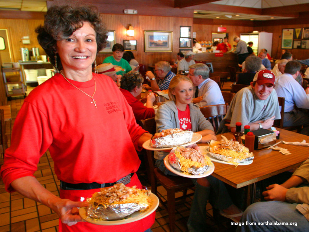Waitress holding plates of food with people at tables eating in background