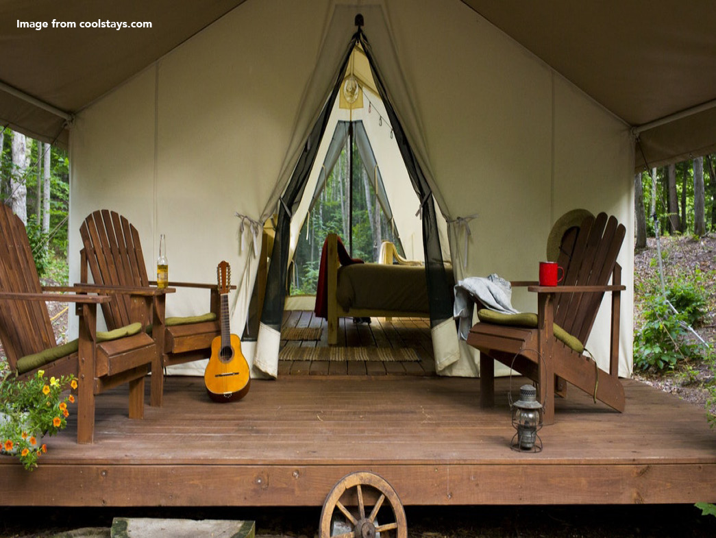 Large canvas tent with wooden porch. Porch has wooden chairs and guitar placed on it.