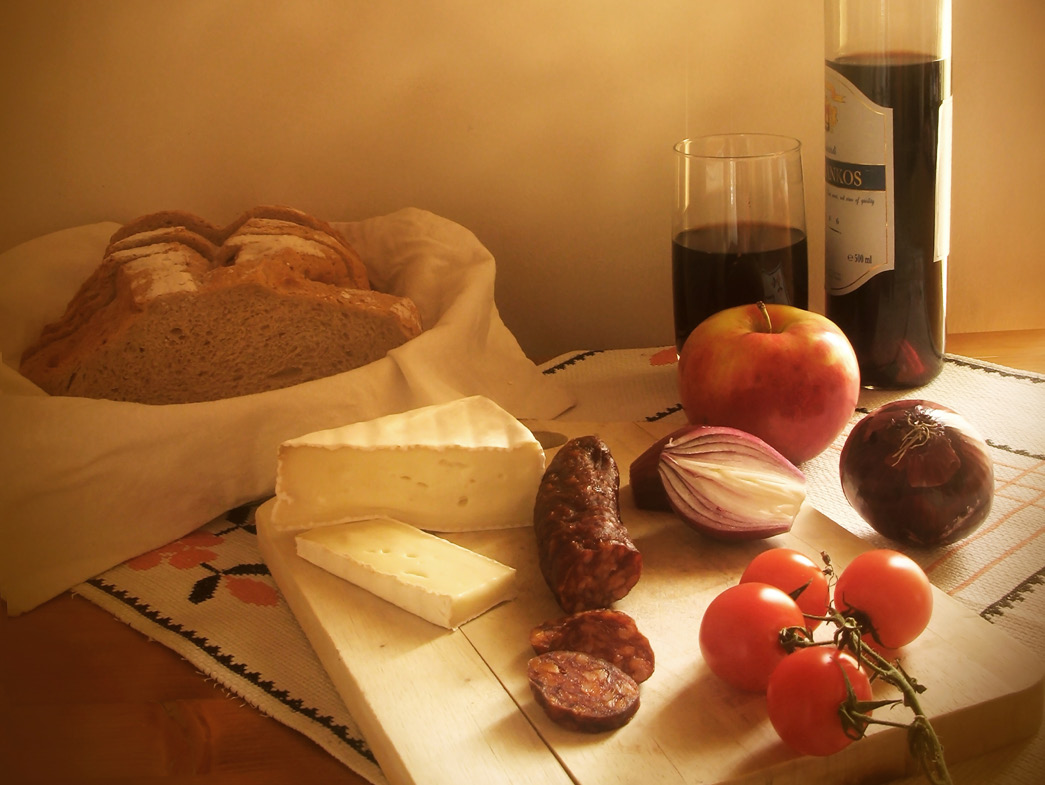 Wine next to basket of bread, with cheese, tomatoes etc. sitting on cutting board